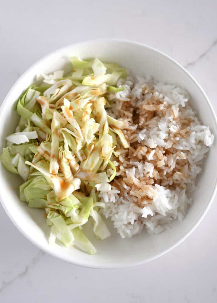 White bowl with chopped cabbage, white rice and Asian-style dressing.