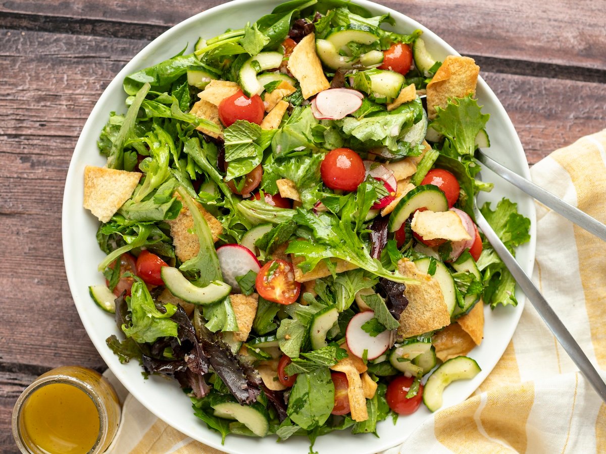 fattoush salad in white bowl with small cup of dressing below it