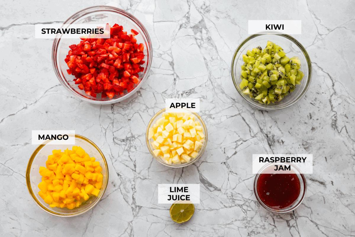 Vibrant fruit salsa is a fresh, juicy twist on your favorite snack! Sweet berries, tropical mango, and a splash of lime always steal the spotlight! Especially when served with crispy cinnamon chips! Overhead shot of labeled ingredients.