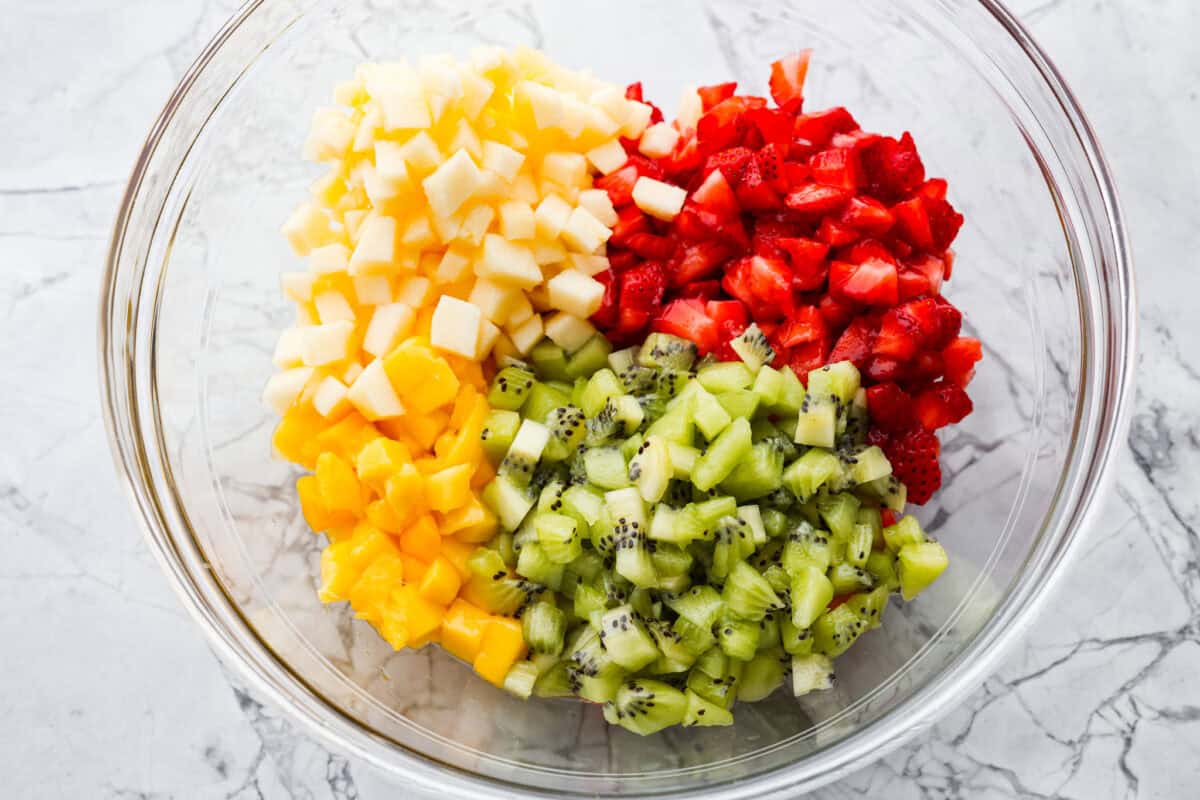 Vibrant fruit salsa is a fresh, juicy twist on your favorite snack! Sweet berries, tropical mango, and a splash of lime always steal the spotlight! Especially when served with crispy cinnamon chips! Diced fruit added to a bowl.