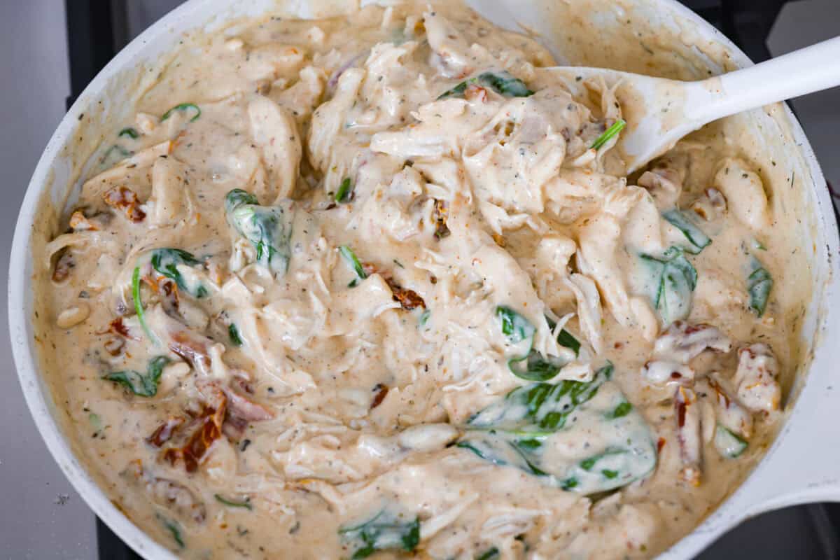 They don’t call it Marry Me Lasagna for nothing! One bite of the creamy sauce, tender chicken, and melty cheese, and everyone will be saying, Someone stirring the chicken and spinach into the sauce.
