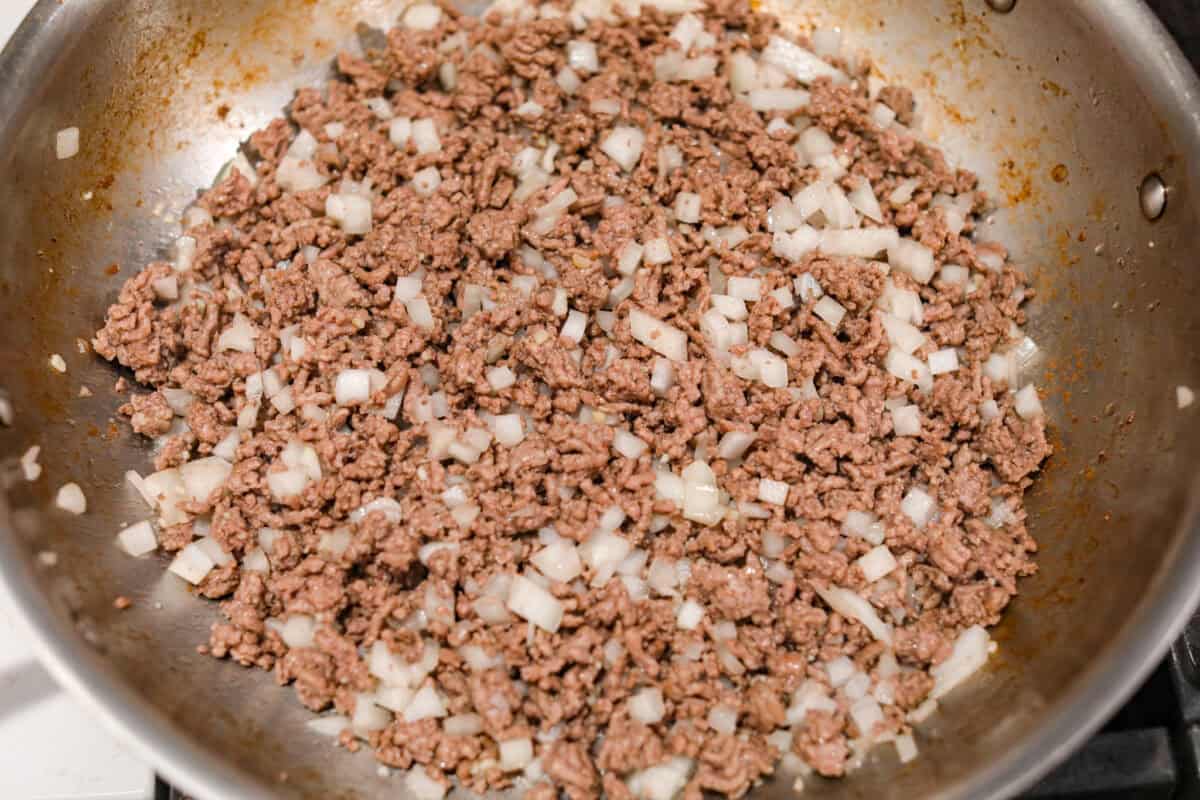 If you love shepherd’s pie, you’ve got to try this Tater Tot Casserole! It’s the ultimate lazy-girl version, with tots instead of mashed potatoes, melty cheese, hearty beef, and total comfort in every bite. The kids will absolutely devour it. Ground beef and onion cooking in a skillet.