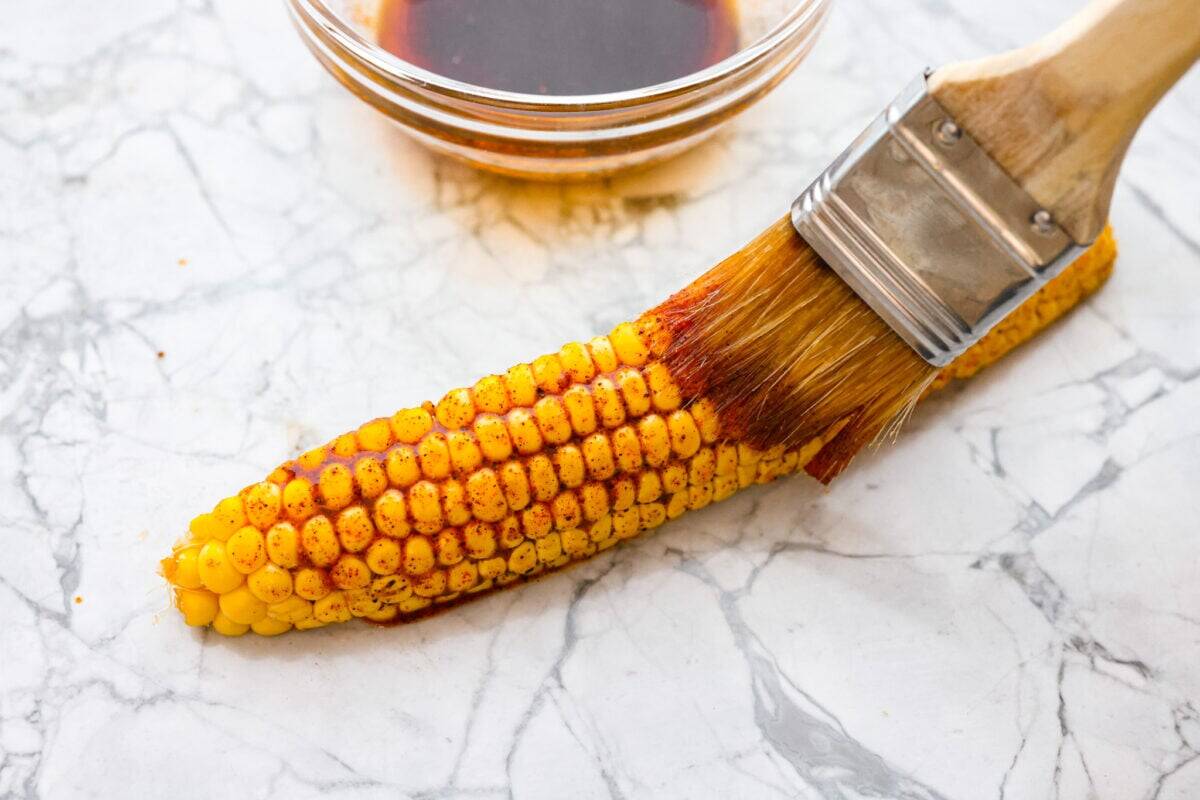 Someone brushing the corn rib with marinade. 
