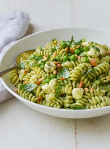 Bowl of pesto pasta salad with pea, pine nuts, and mozzarella pearls.