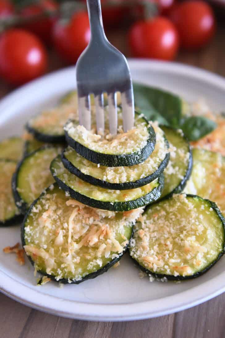 Fork spearing three zucchini rounds on gray plate.
