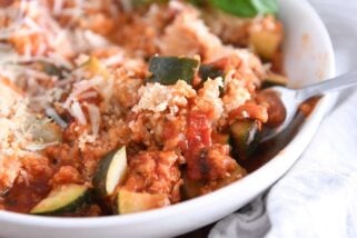 Fork taking bite of zucchini, chicken, panko, tomato sauce and cheese.