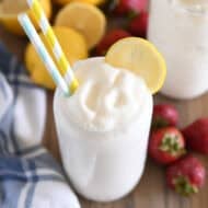 Tall glass filled with frosted lemonade with striped straws and lemon slice for garnish.