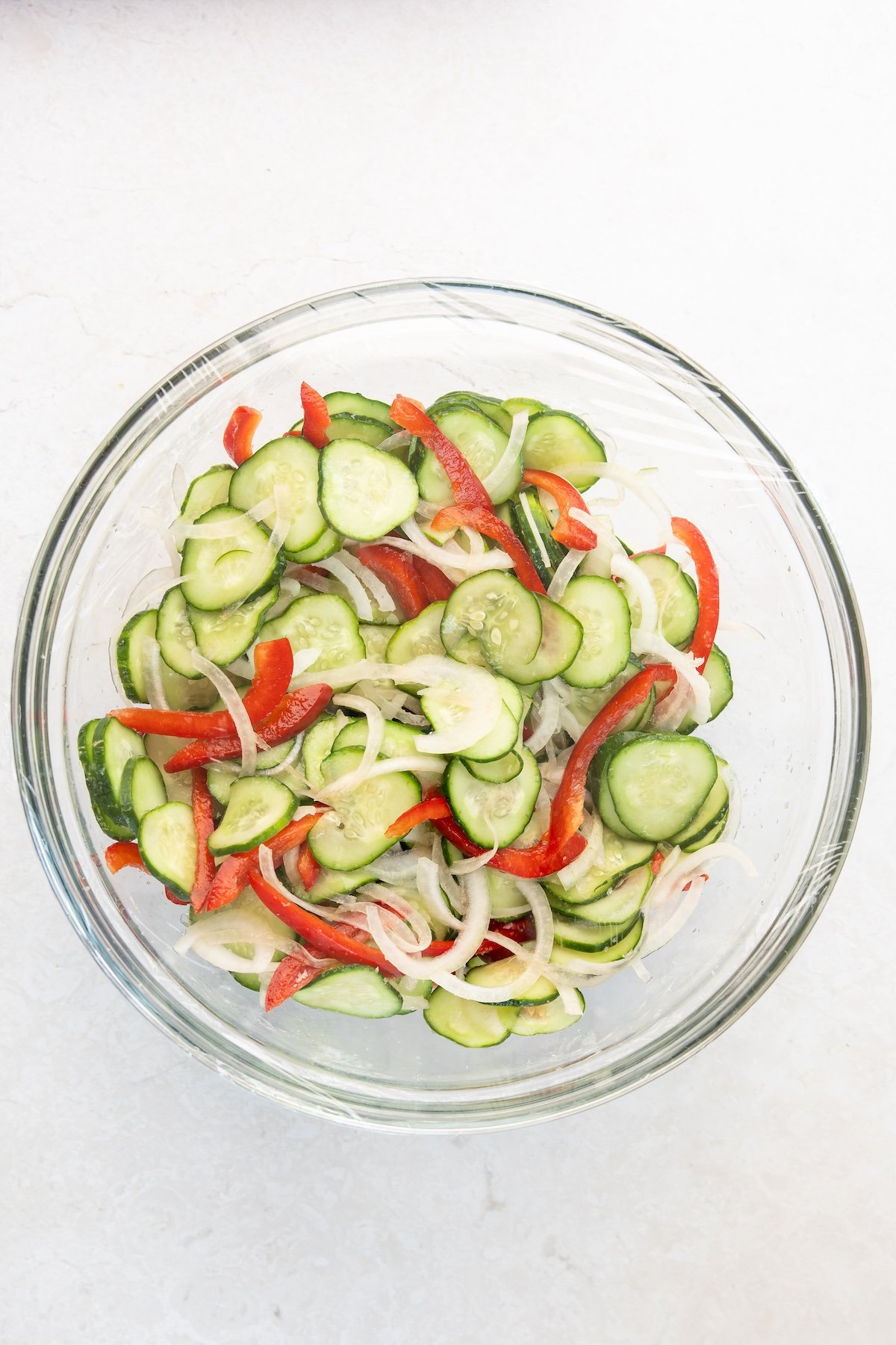 large glass bowl with cucumbers, onions, and bell pepper tossed in salt
