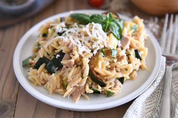 Orzo with tuna, zucchini, and Parmesan with fresh basil as a garnish on gray plate.