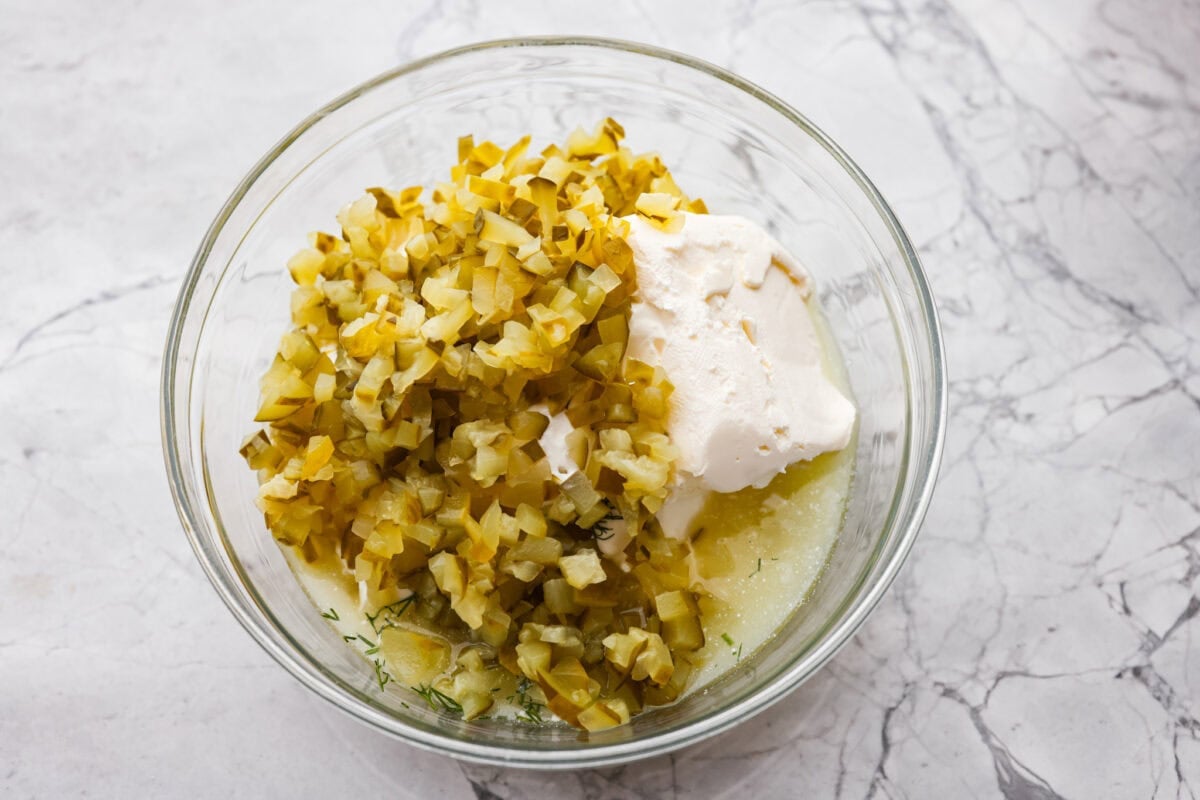 Chopped pickles and other ingredients added to a bowl. 