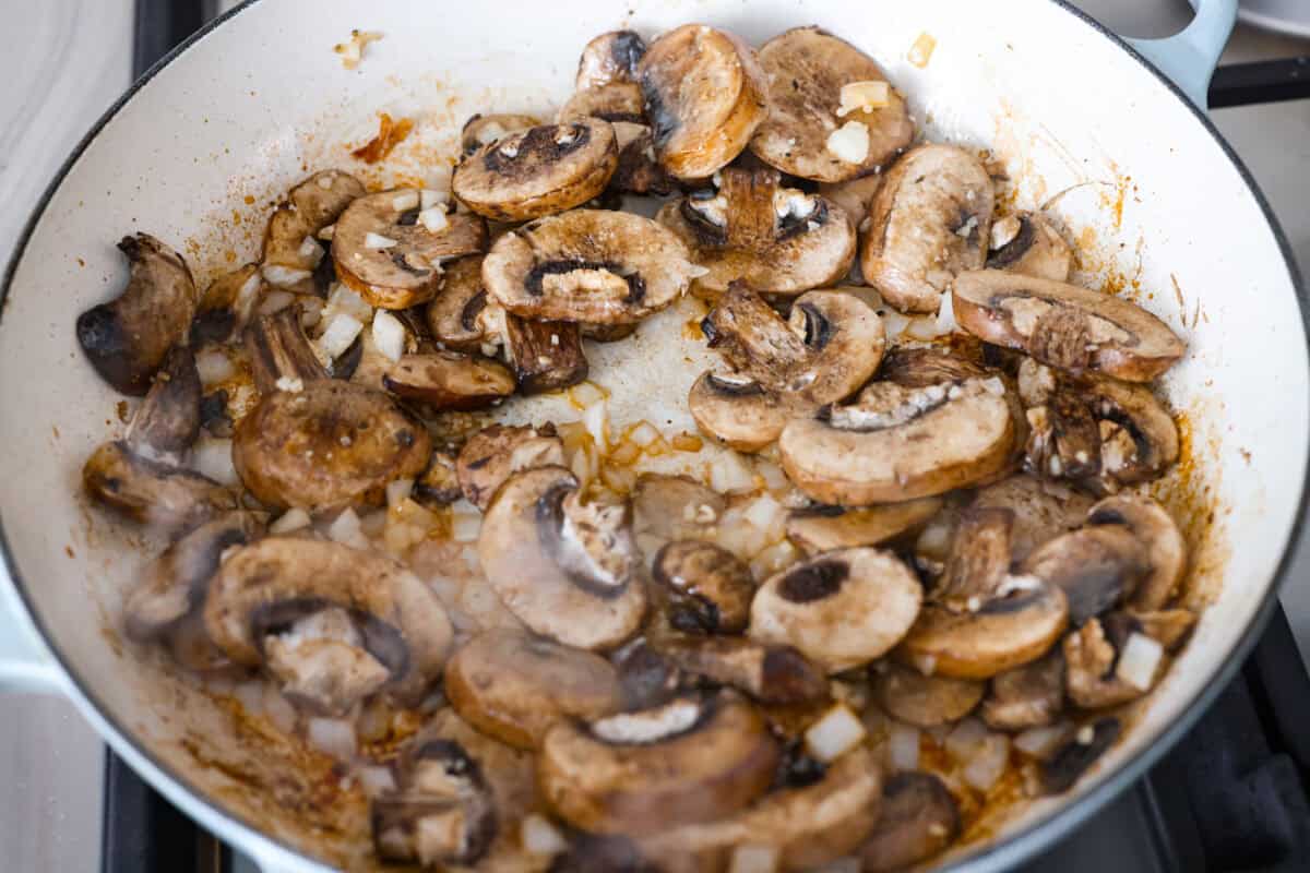 Mushrooms, onions, and garlic cooking in a skillet.