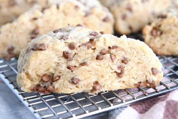 Side view of a baked cinnamon chip scone on a wire cooling rack with more scones behind it.