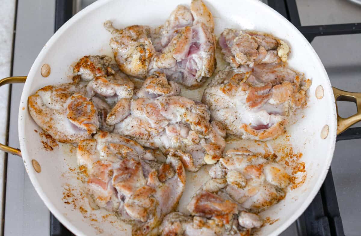 Apple cider chicken thighs bring all the best fall flavors to your plate! Juicy chicken, caramelized apples, and a rich cider sauce for the ultimate cozy dinner. Chicken thighs browned and cooking in a skillet.