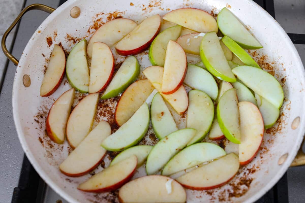 Apple cider chicken thighs bring all the best fall flavors to your plate! Juicy chicken, caramelized apples, and a rich cider sauce for the ultimate cozy dinner. Apple slices in the skillet cooking.