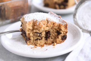 Half eaten square of chocolate chip cake dusted with powdered sugar on white plate.