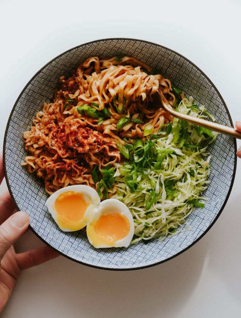Sesame butter noodles in a bowl with cabbage salad and egg.