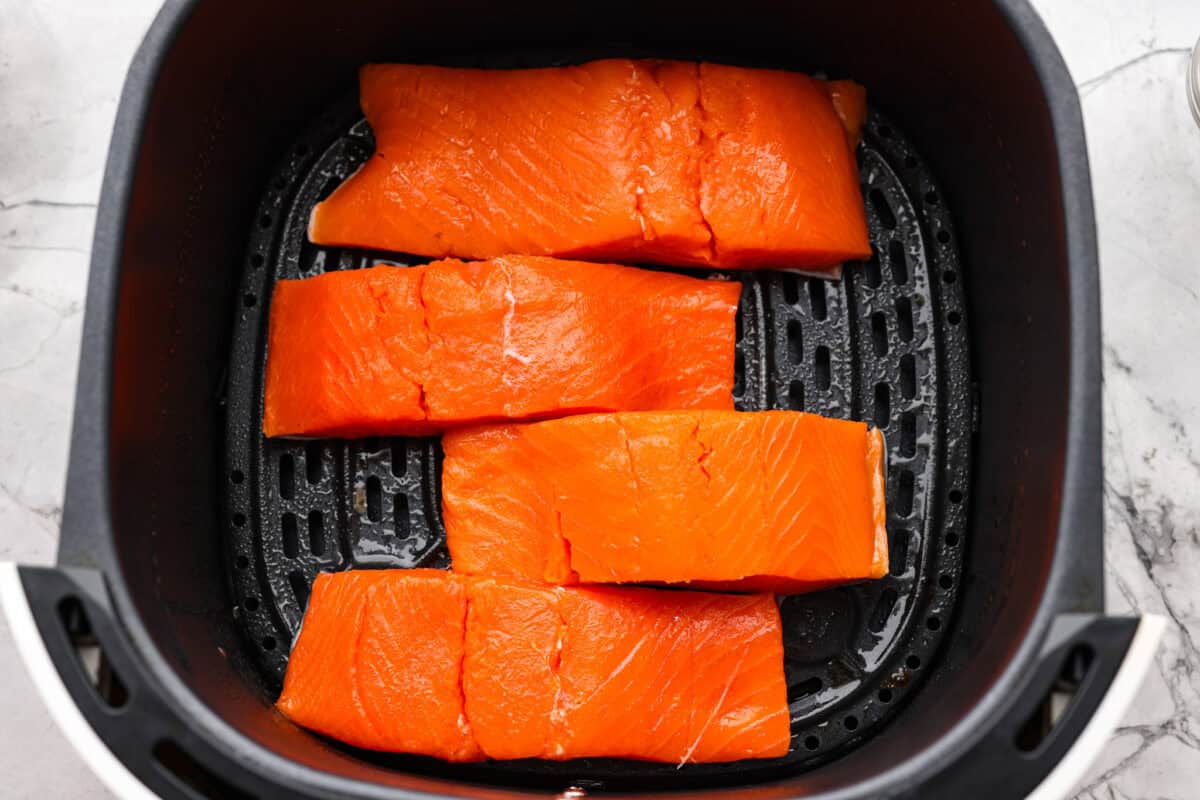 Salmon fillets skin side down in the bottom of the air fryer basket.