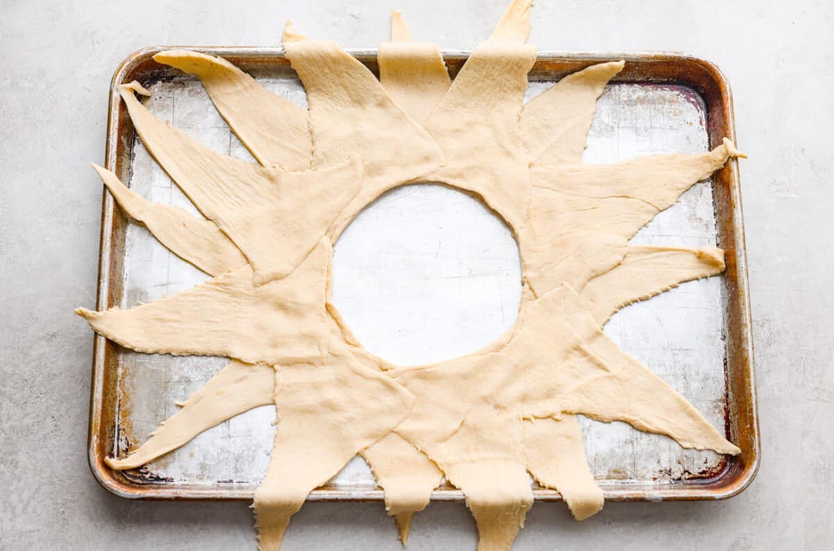 Triangles of crescent dough arranged in a sunburst shape on a cookie sheet.