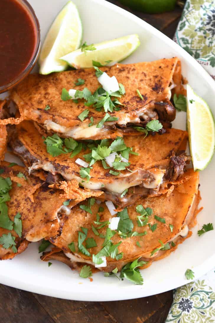 Three corn tortillas filled with beef and melty cheese topped with cilantro and onions on white platter.