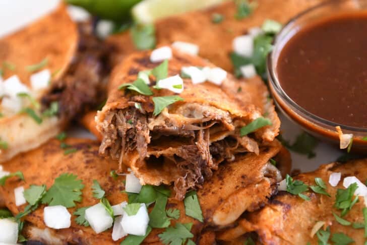 Birria taco with beef and melted cheese split in half on white tray cilantro and white onions.