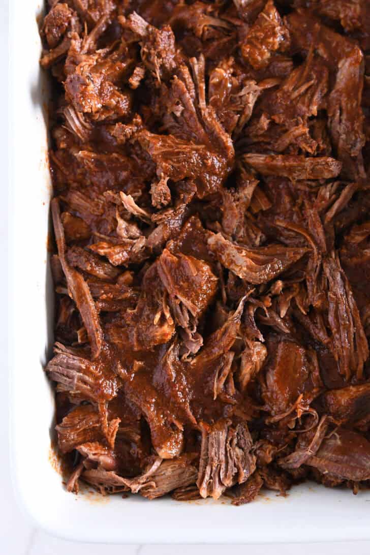 White 9X13-inch pan with shredded Mexican birria beef and broth.