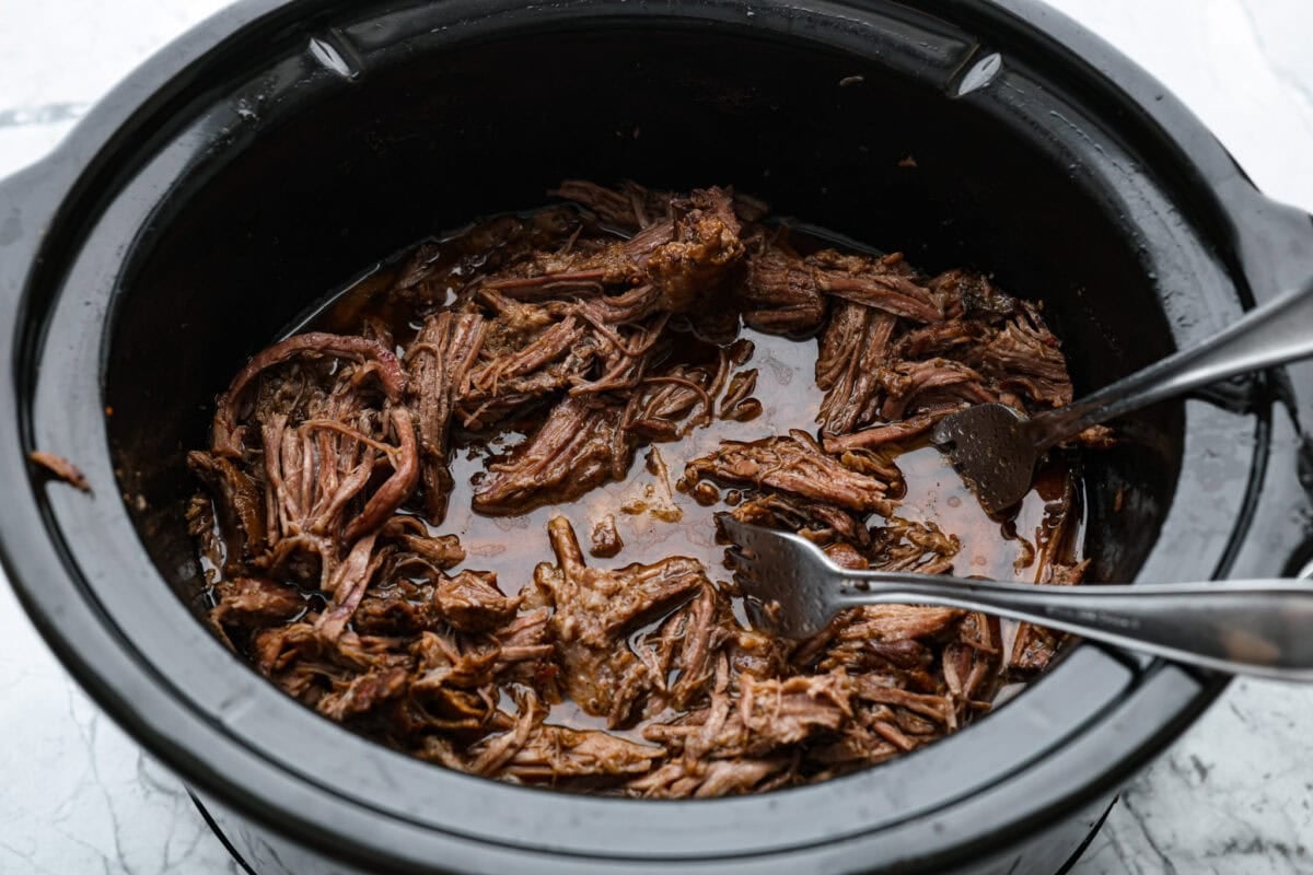 Pot roast cooked and someone is shredding it with forks. 