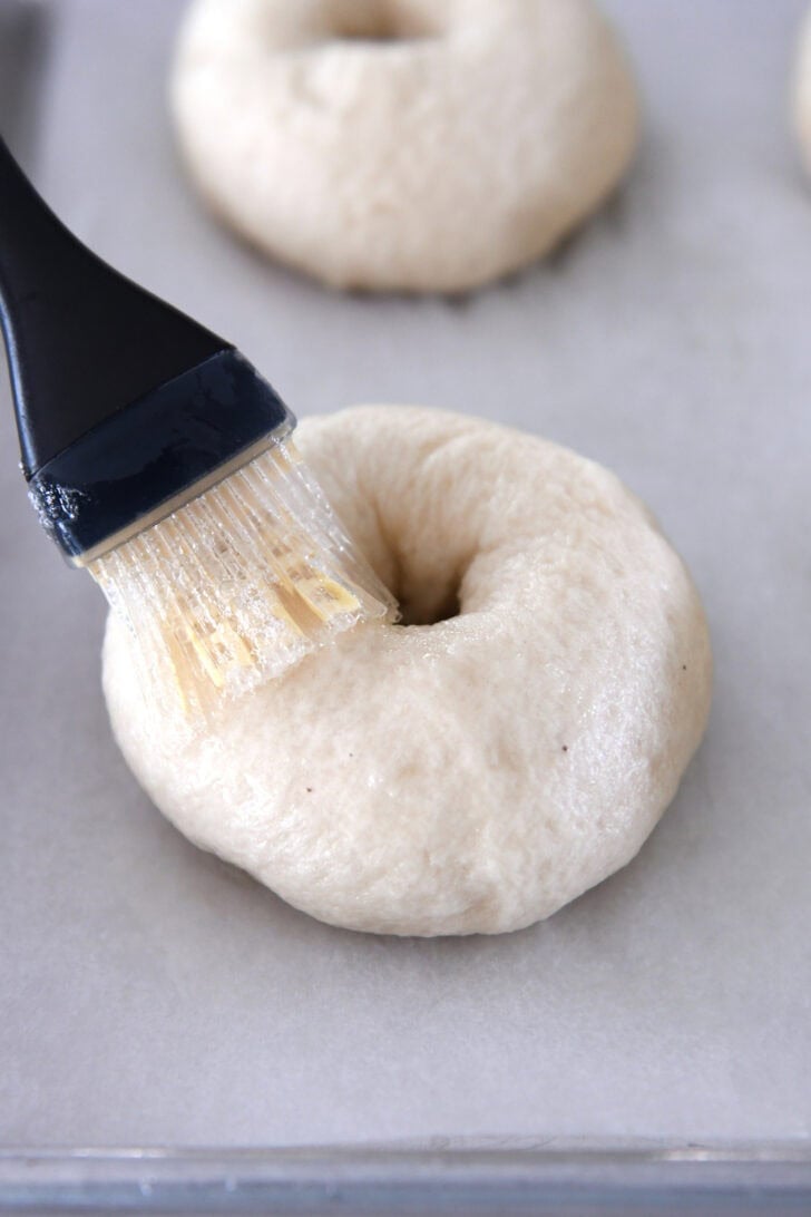 Brushing egg wash on boiled bagel before baking.