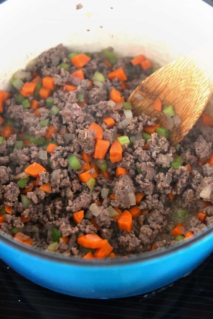 Enameled cast iron pot with cooked ground beef, carrots, and celery.