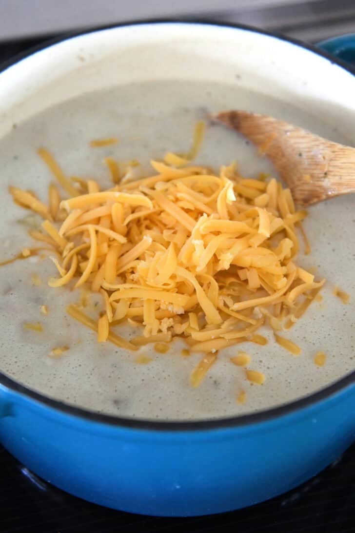 Enameled cast iron Dutch oven with creamy soup and pile of shredded sharp cheddar in the center.