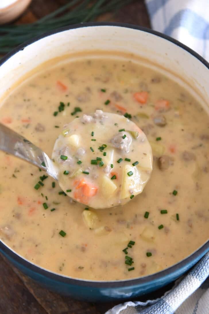 Ladle with scoop of creamy cheesy soup with potatoes, hamburger, and carrots and sprinkled with fresh chives.