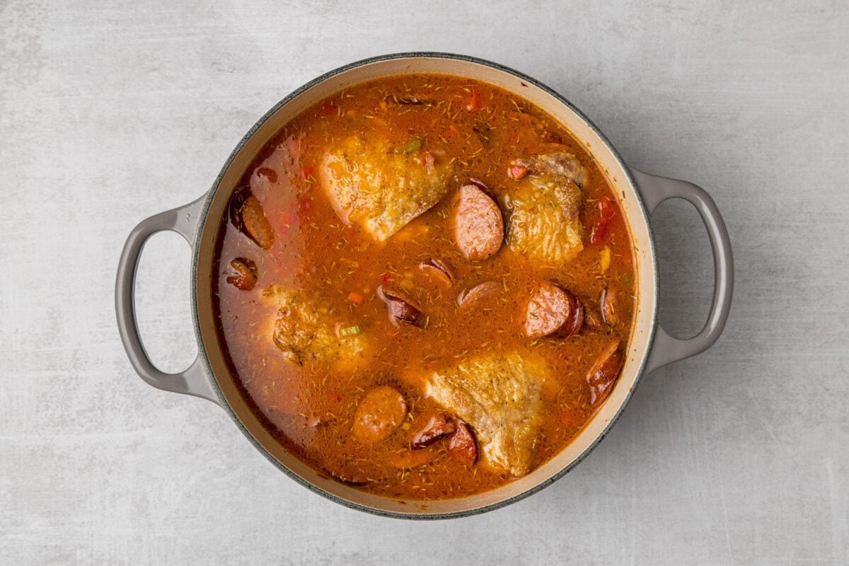 dutch oven with browned chicken and sausage and chicken broth, clam juice, diced tomatoes, thyme, and cayenne pepper