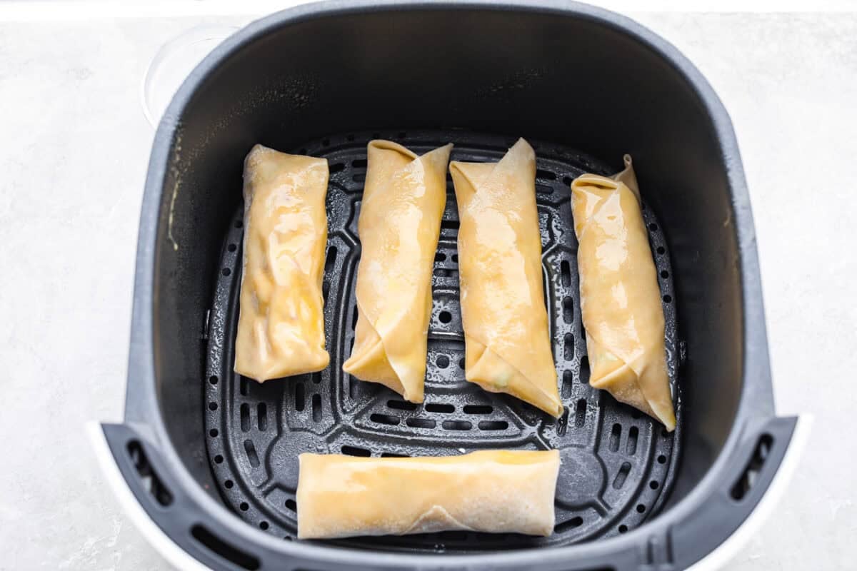 Egg rolls spaced evenly in the bottom of the air fryer basket. 