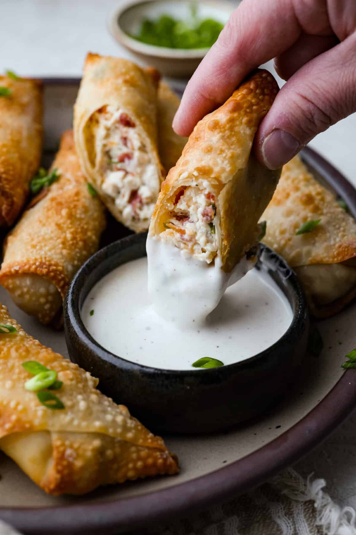 Someone dipping a crack chicken egg roll into ranch dressing.