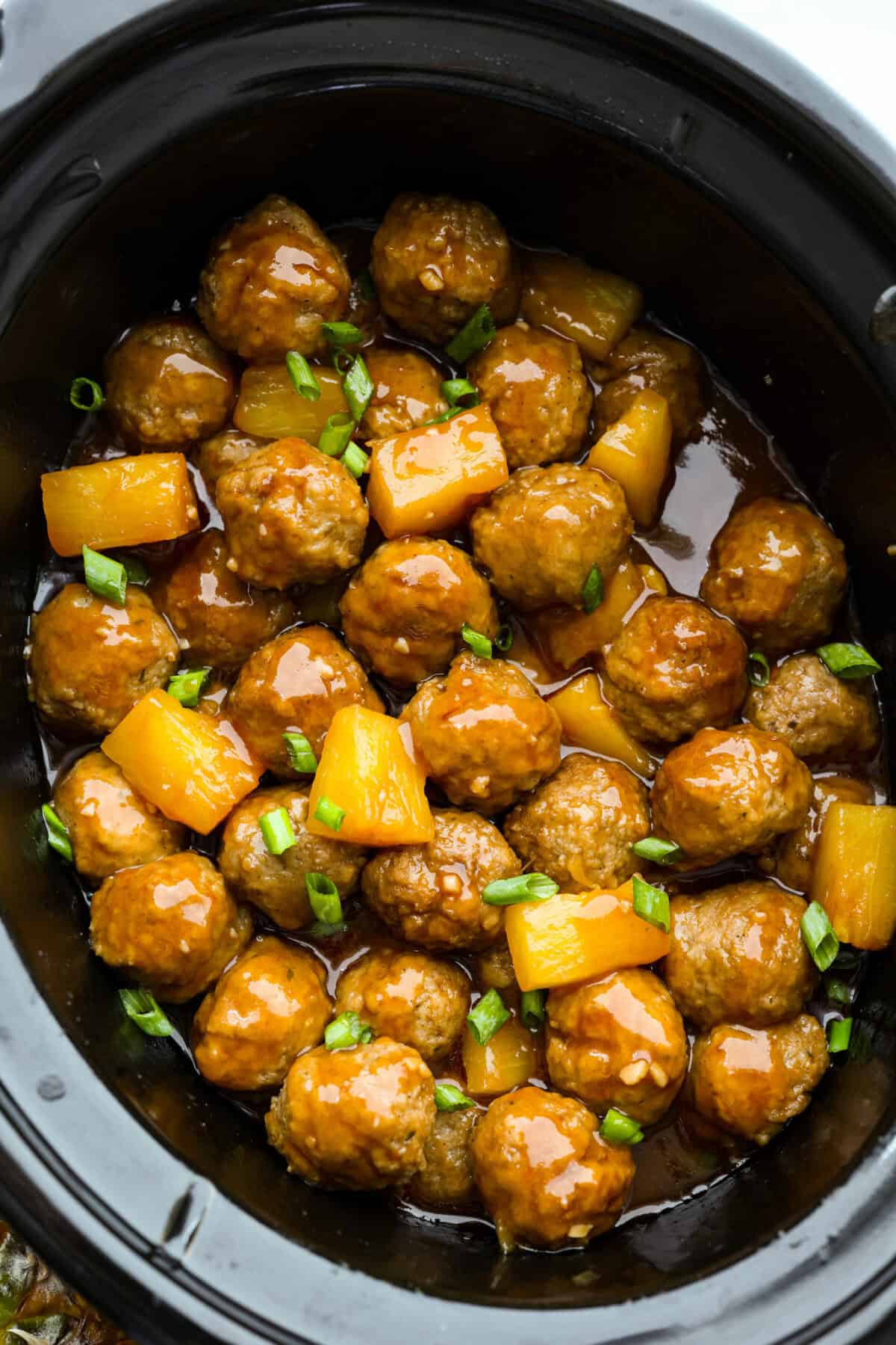 Crockpot huli huli meatballs in sauce garnished with green onions.