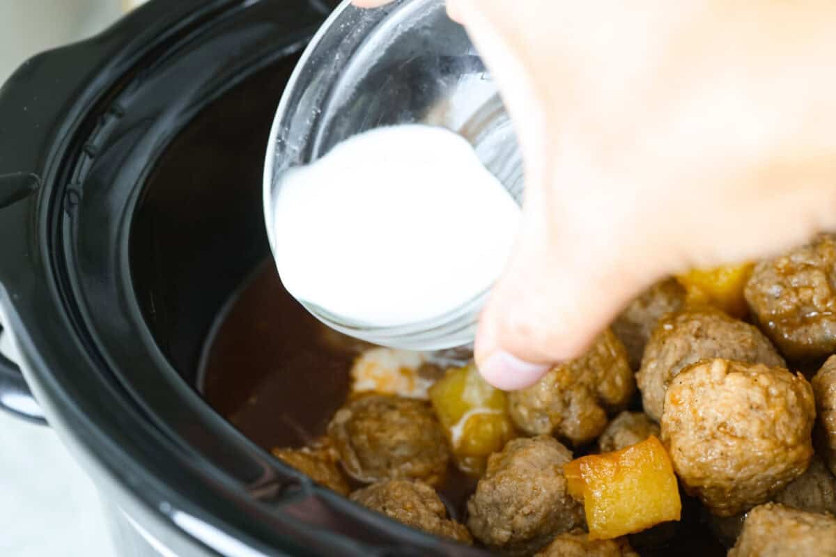 Cornstarch slurry being added to the crockpot to thicken the sauce. 