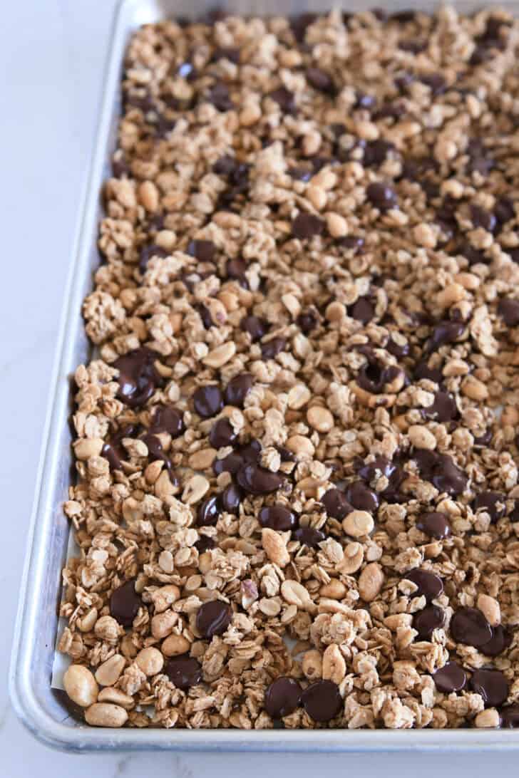 Melted chocolate chips tossed in with baked peanut butter granola on parchment lined half sheet pan.