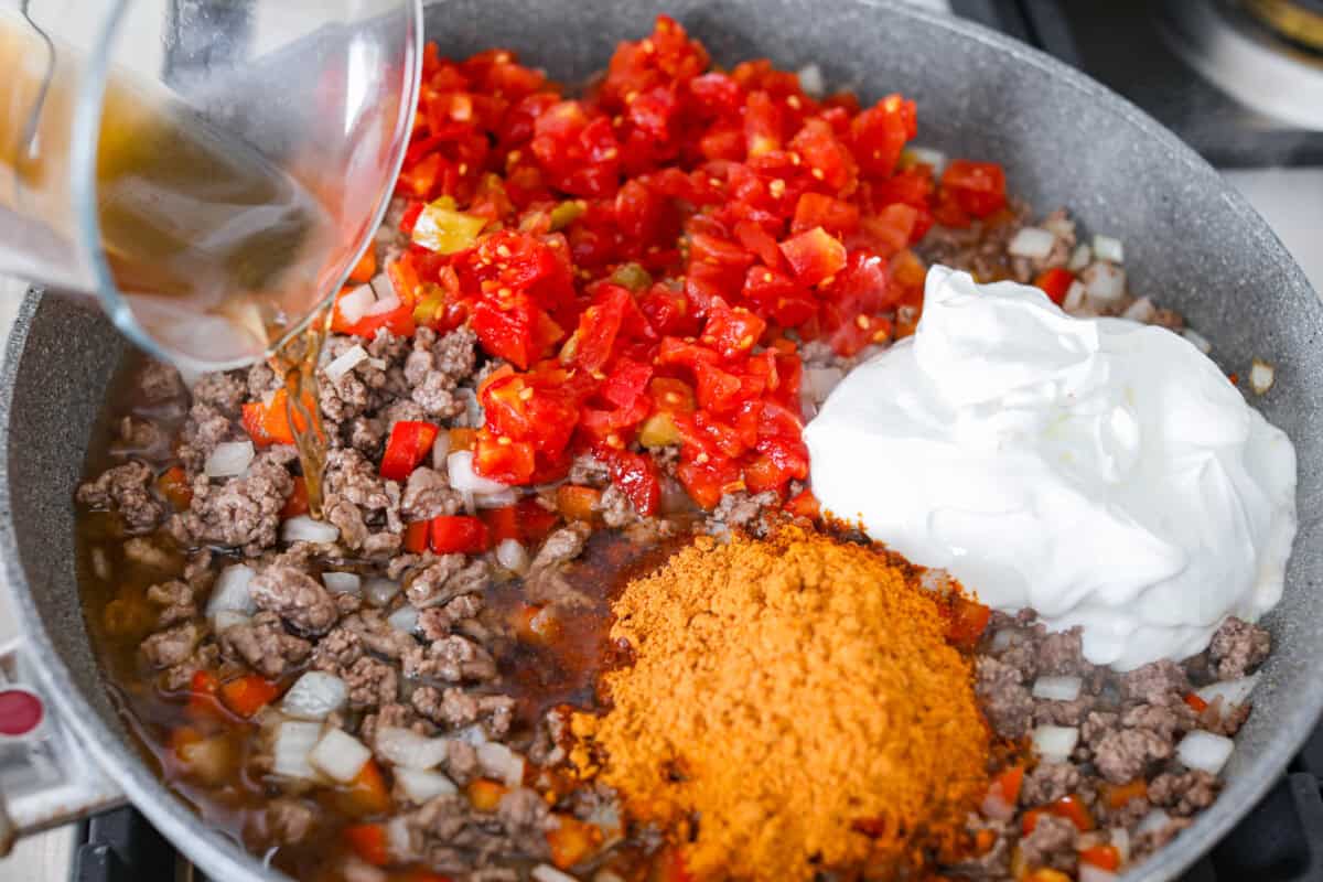Tomatoes, sour cream, broth, and seasonings added to the meat mixture in the skillet.