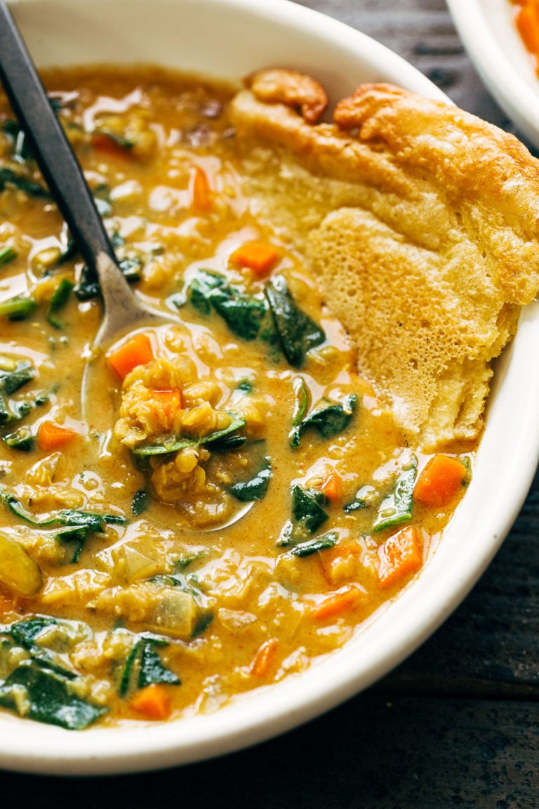 Red lentil soup in a bowl with socca on the side.