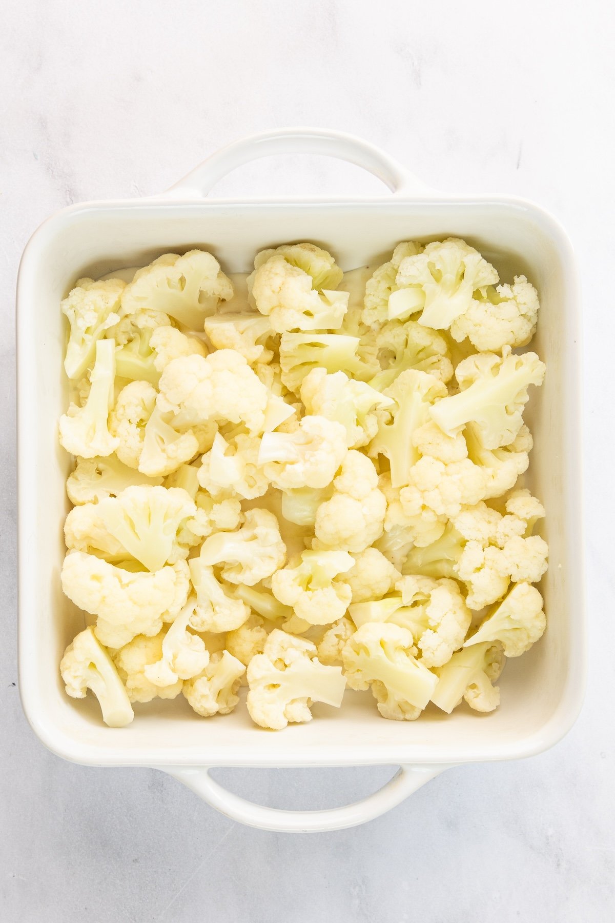 8-inch square baking dish with cauliflower on top of bechamel sauce