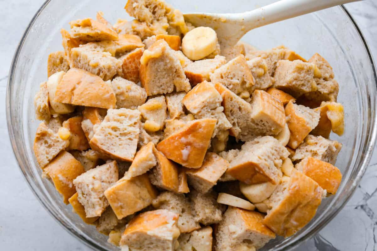 Someone stirring the milk mixture into the bread and bananas. 