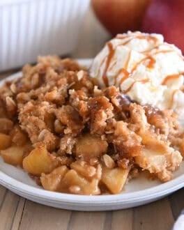 Serving of caramel apple crisp on gray plate with ice cream also drizzled with caramel.