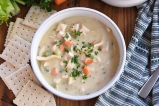 Top down view of creamy chicken noodle soup with saltine crackers on the side.