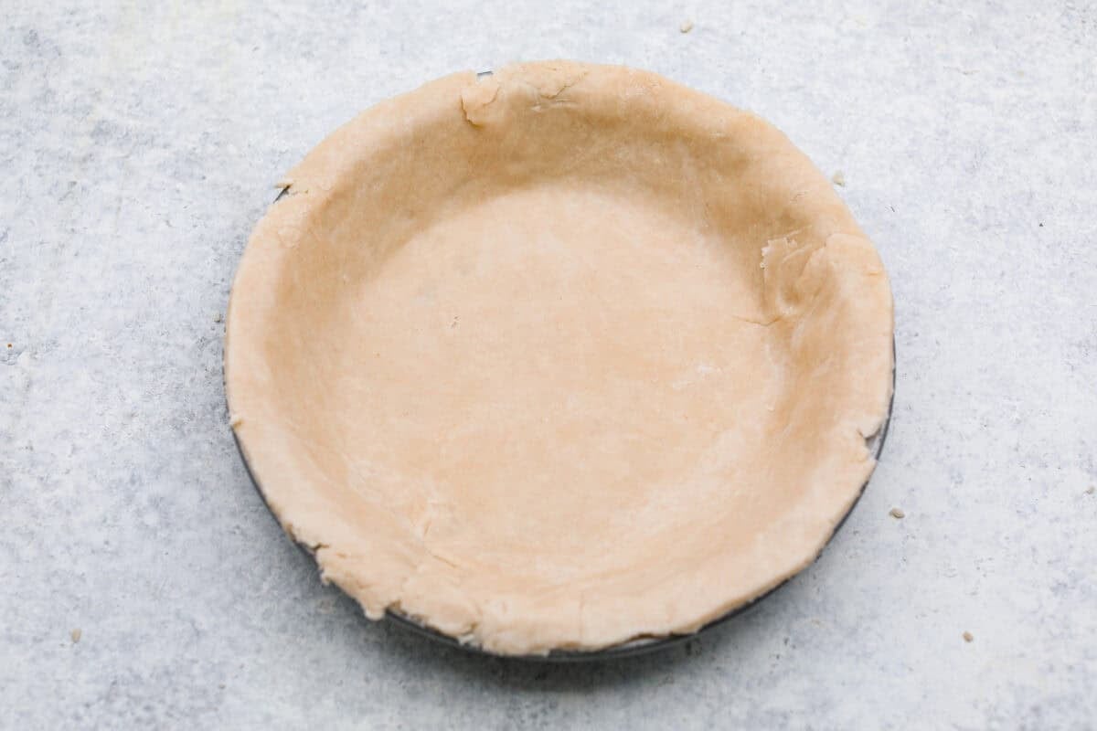 Rolled out dough placed into a pie tin. 