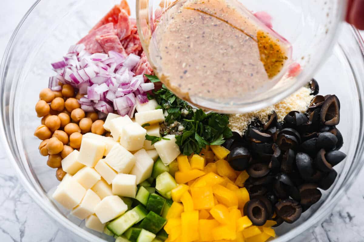 Someone pouring the dressing over the large bowl of salad ingredients.