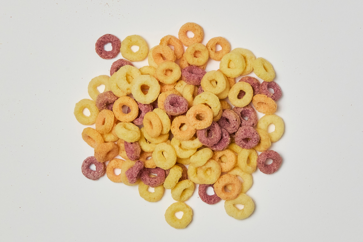 Pile of colorful fruity cereal hoops. Breakfast cereal, snack food. Yellow, orange, and purple loops.