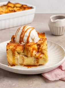 slice of bread pudding on plate topped with vanilla ice cream and caramel sauce