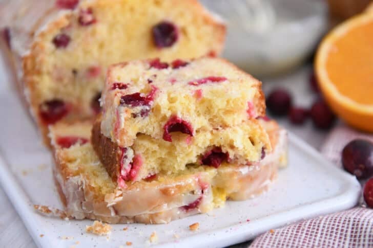 One slice of cranberry orange bread in half on top of full slice on white tray.
