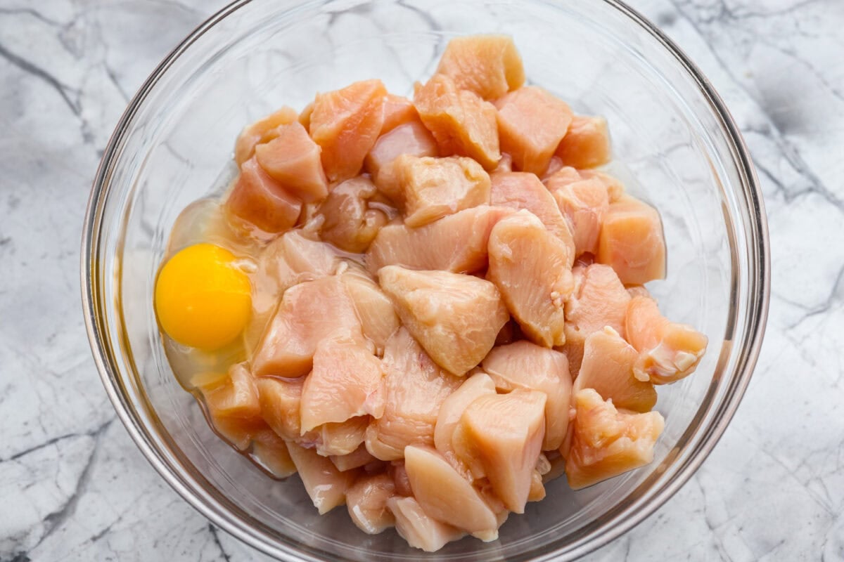 Bowl of cut up chicken with an egg. 
