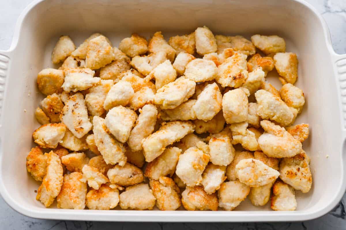 Browned chicken added to a baking dish.
