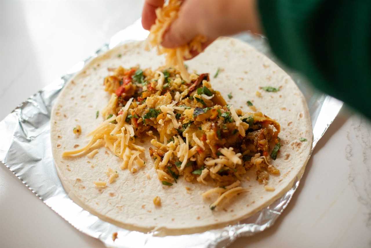 Sprinkling cheese on a breakfast burrito.